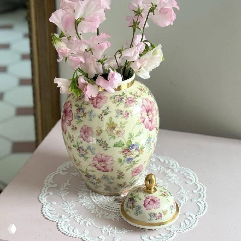 Текстиль с цветочным принтом и кружевной отделкой в интерьере; кадр содержит цифровые искажения, виден узор ткани и цветочные мотивы.