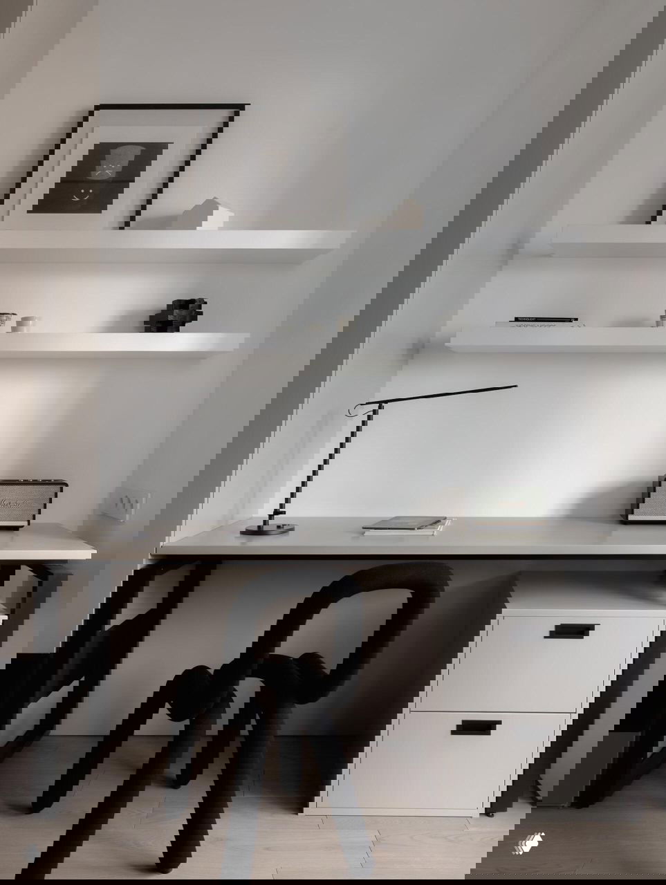 Минималистичное рабочее место с тонким столом, белыми настенными полками и чёрным дизайнерским стулом-скульптурой; спокойная рабочая зона в общем стиле квартиры.