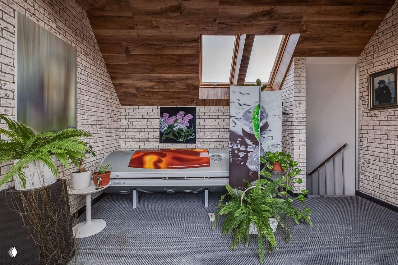 Зона с солярием и декоративными перегородками, белая кирпичная отделка стен, рядом размещены папоротники и небольшие столики для растений.