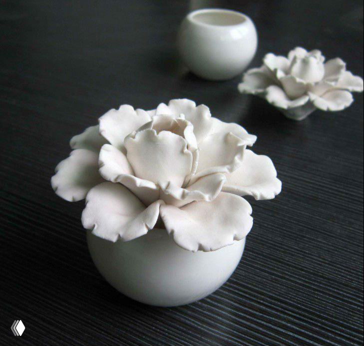 Небольшая фигурная композиция из бисквитного фарфора в виде цветка на тёмной фактурной поверхности, крупный план декоративного матового изделия.