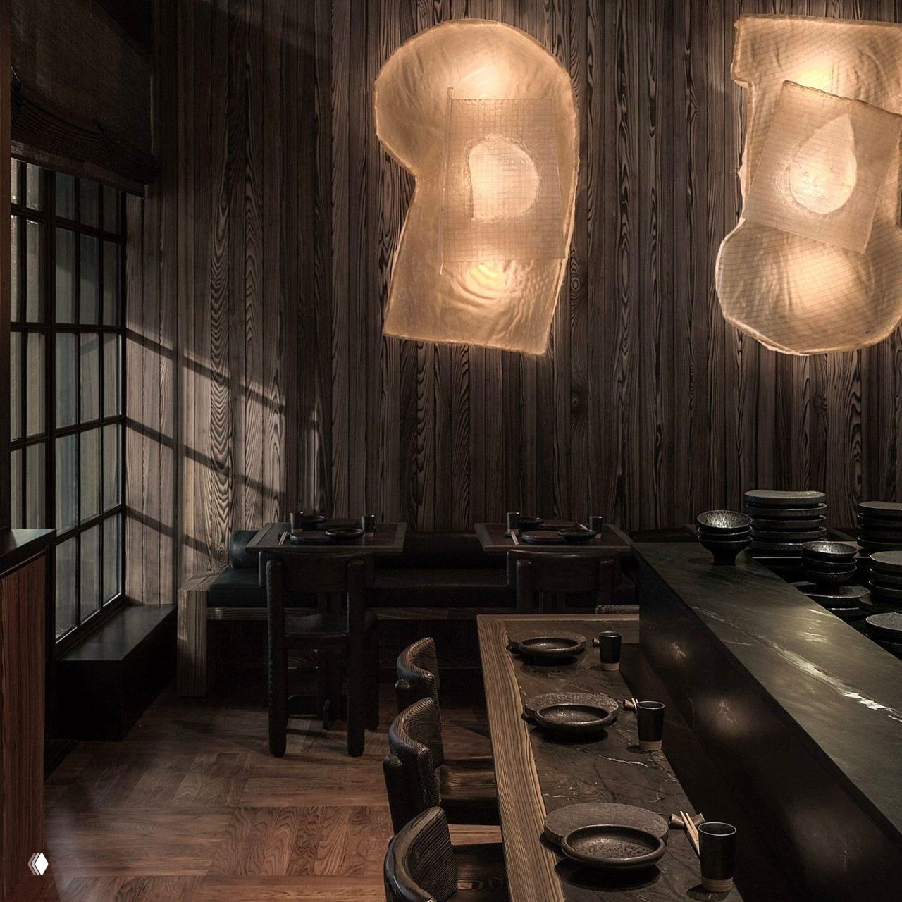 Барная зона и открытая кухня ресторана: тёмная столешница, керамическая посуда и крупные текстильные подвесные светильники над зоной сервировки.