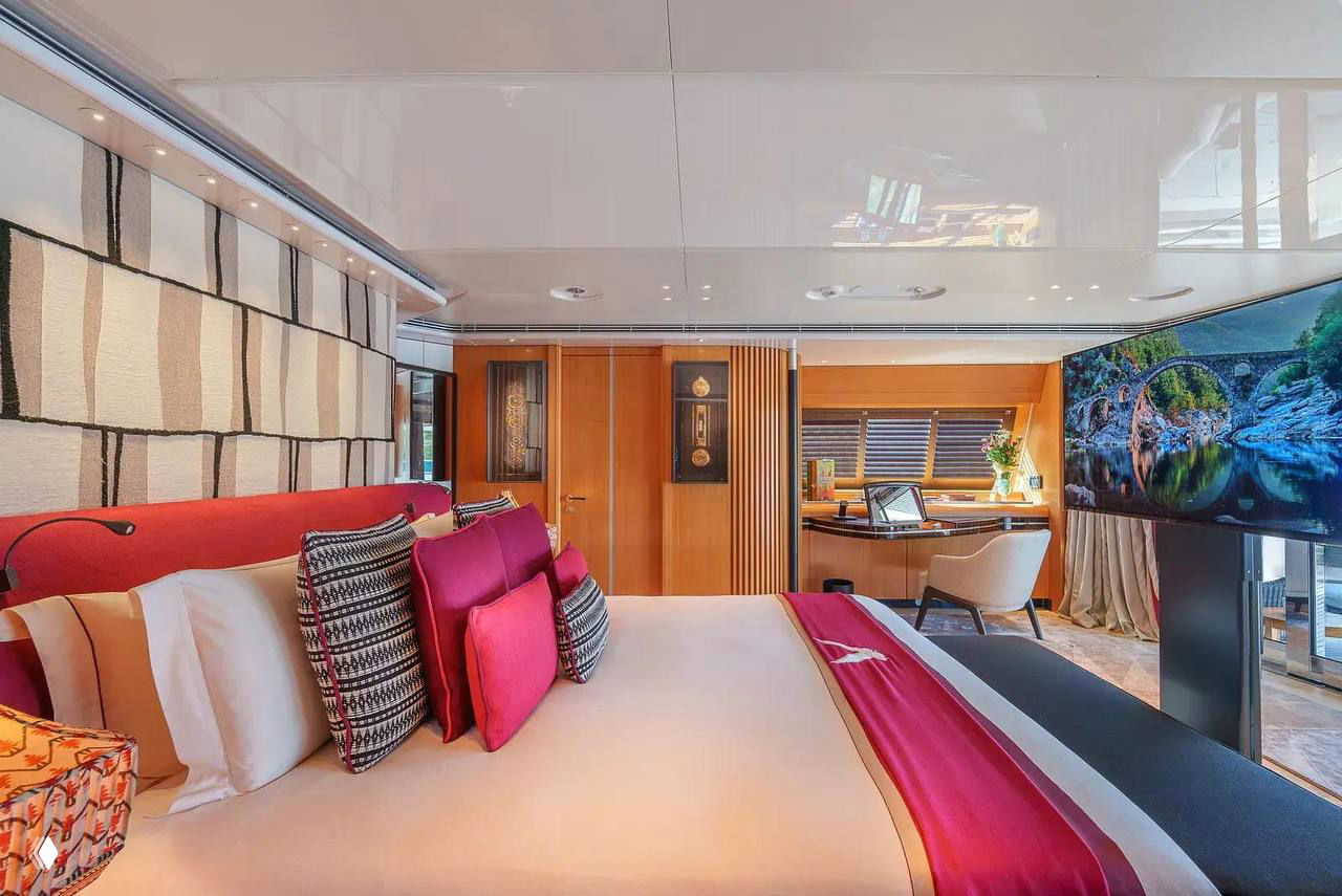 Интерьер мастер-каюты на Maltese Falcon: большая двуспальная кровать с декоративными подушками, рабочая зона и панорамное окно с дневным светом.