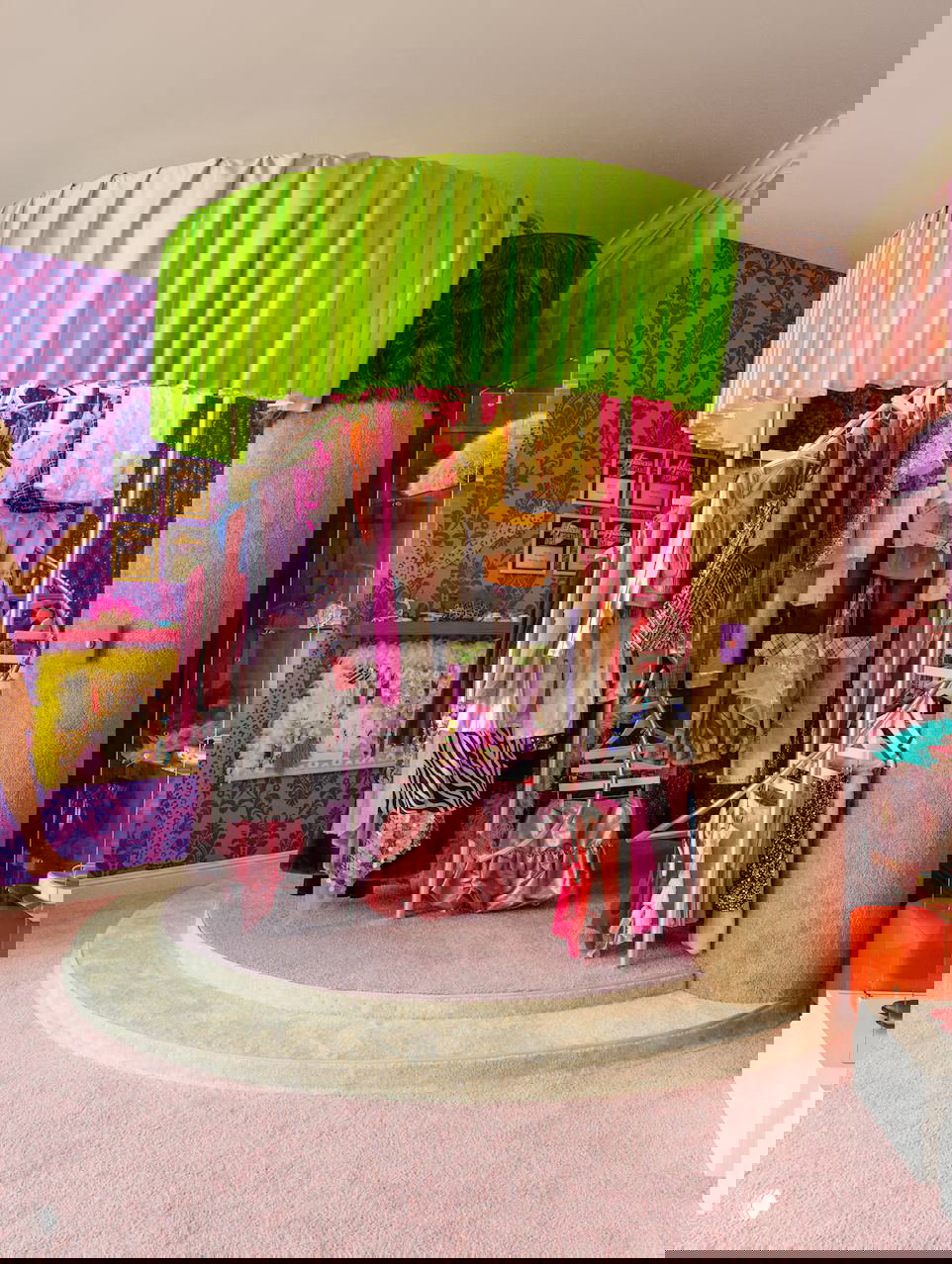 Интерьер гардеробной, стилизованной под «Ханну Монтану»: круглая демонстрационная стойка с яркими сценическими костюмами и розовым ковровым покрытием.