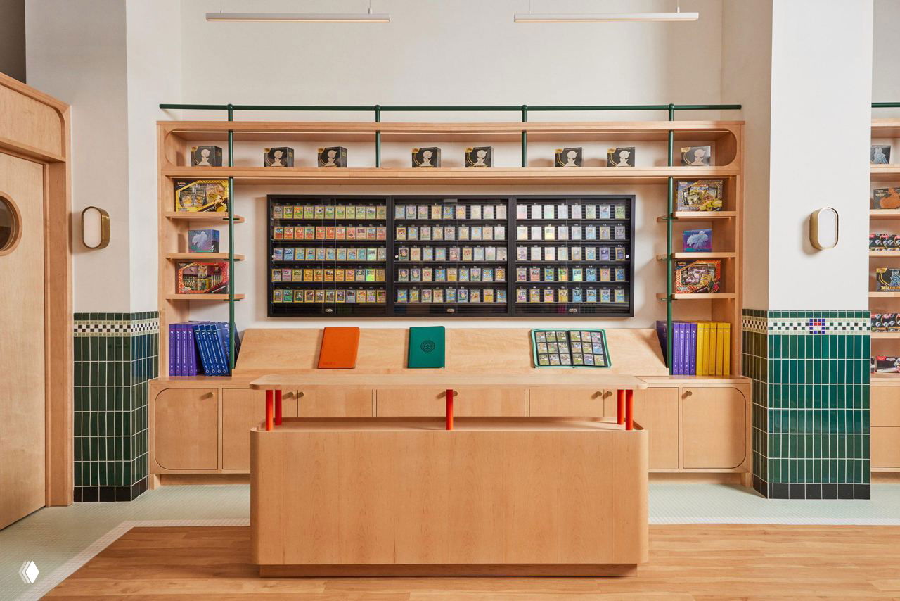 Рабочая зона и демонстрационные шкафы с коллекционными карточками за стеклом, светлое деревянное оформление и зелёная плитка по периметру интерьера.