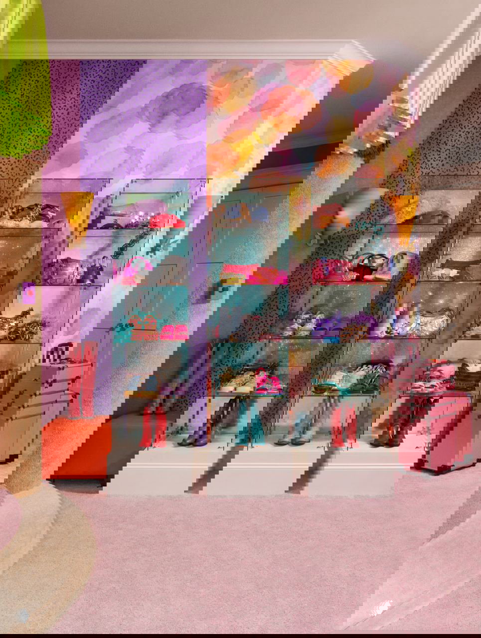 Стеклянные витрины с обувью и аксессуарами на фоне разноцветных акварельных обоев и пурпурных декоративных панелей в тематическом интерьере.