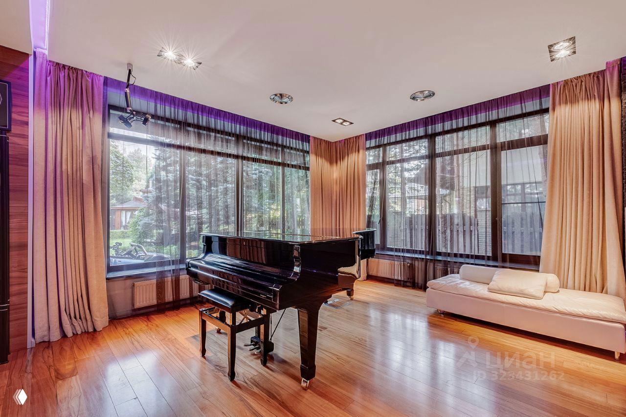 Светлая музыкальная комната с роялем на паркетном полу, большими окнами в пол и мягким естественным освещением, аккуратная мебель по периметру.