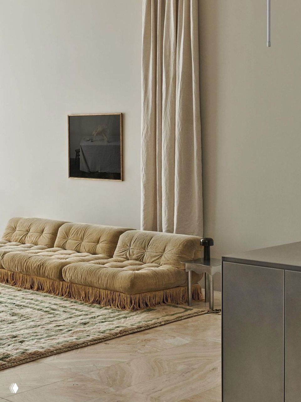 Низкий бежевый модульный диван с длинной бахромой в минималистичной светлой комнате; простая декоративная картина и высокие шторы усиливают спокойную палитру.