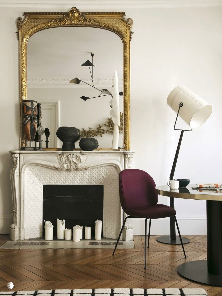 Крупный план потолочной розетки и филигранной лепнины в сочетании с каркасной металлической люстрой, декоративный рельеф на фоне светлого потолка.