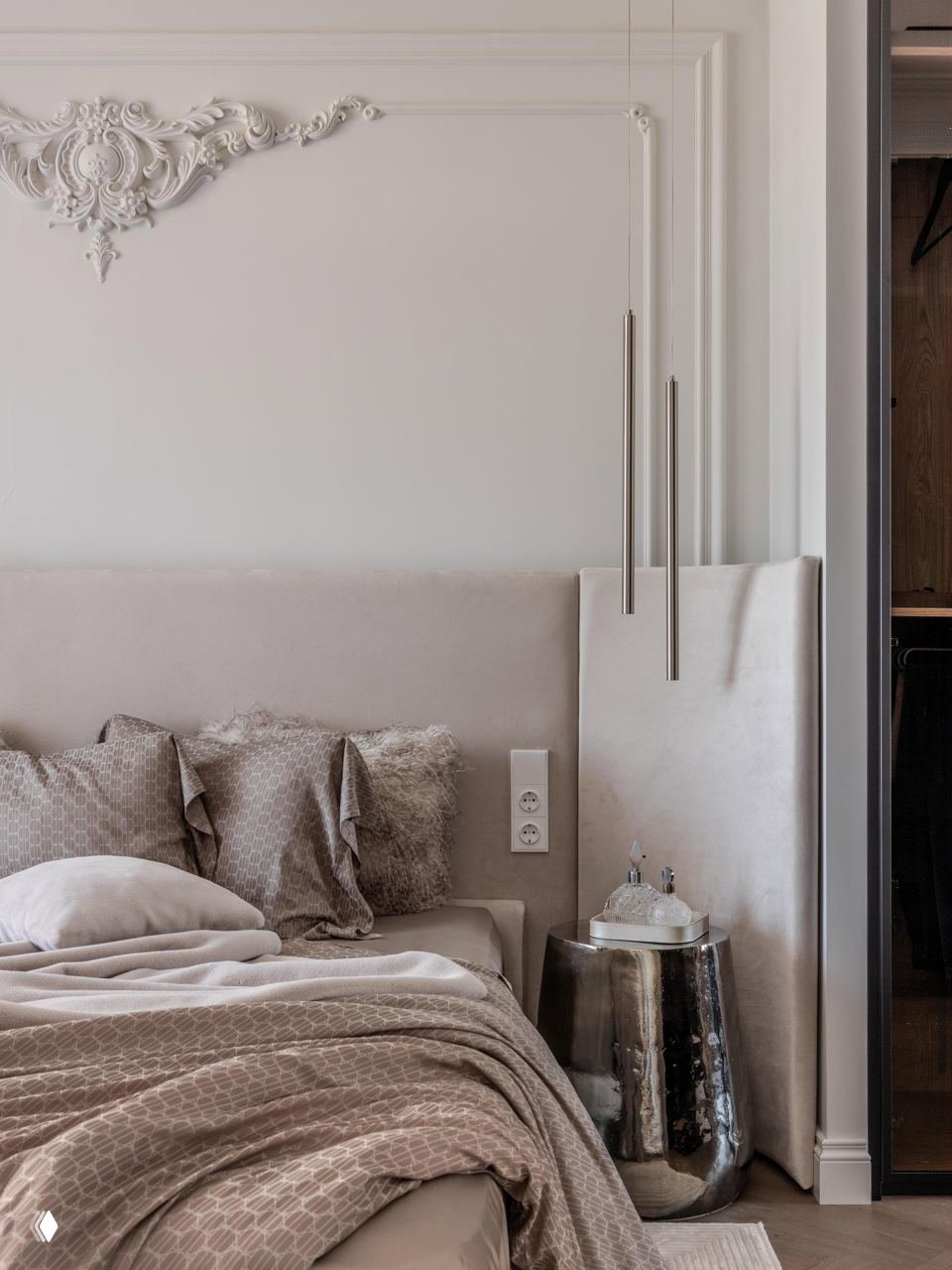 Интерьер спальни: бархатное изголовье в бежевых тонах, декоративные подушки и металлический глянцевый приставной столик