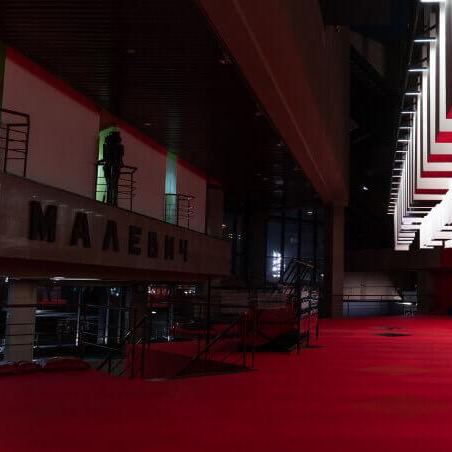 Тёмное или ночное фойе с красным ковровым покрытием и крупным пространственным залом, видна часть фасада и архитектурные детали внутри галерейного комплекса