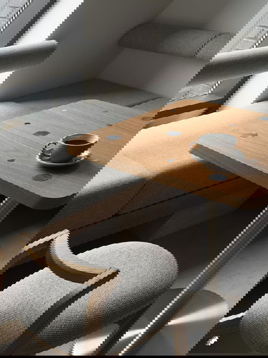 Близкий план деревянного столика и мягкого дивана с чашкой кофе на столе; текстуры ткани и дерева в минималистичном интерьере кофейни Plain в Москве.