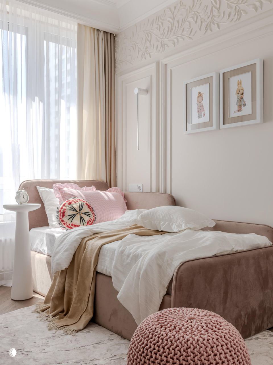 Детская спальня в пастельных оттенках: мягкая розовая кровать, воздушные шторы, декоративные подушки и вязаный пуф у окна