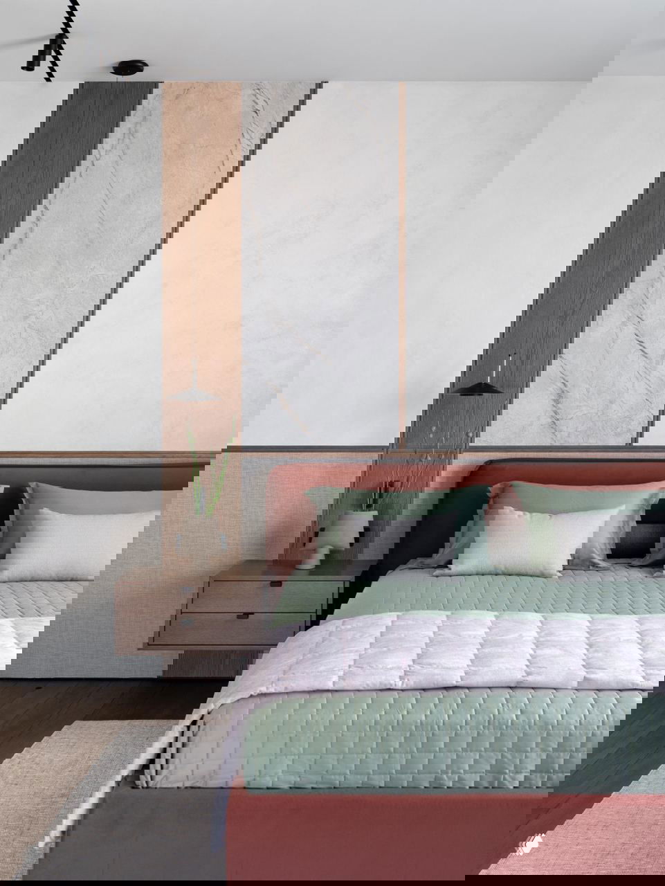 Крупный план изголовья кровати в спальне: мягкая обивка, декоративные подушки и панно из дерева и камня, подчёркивающие композиционный смысл.