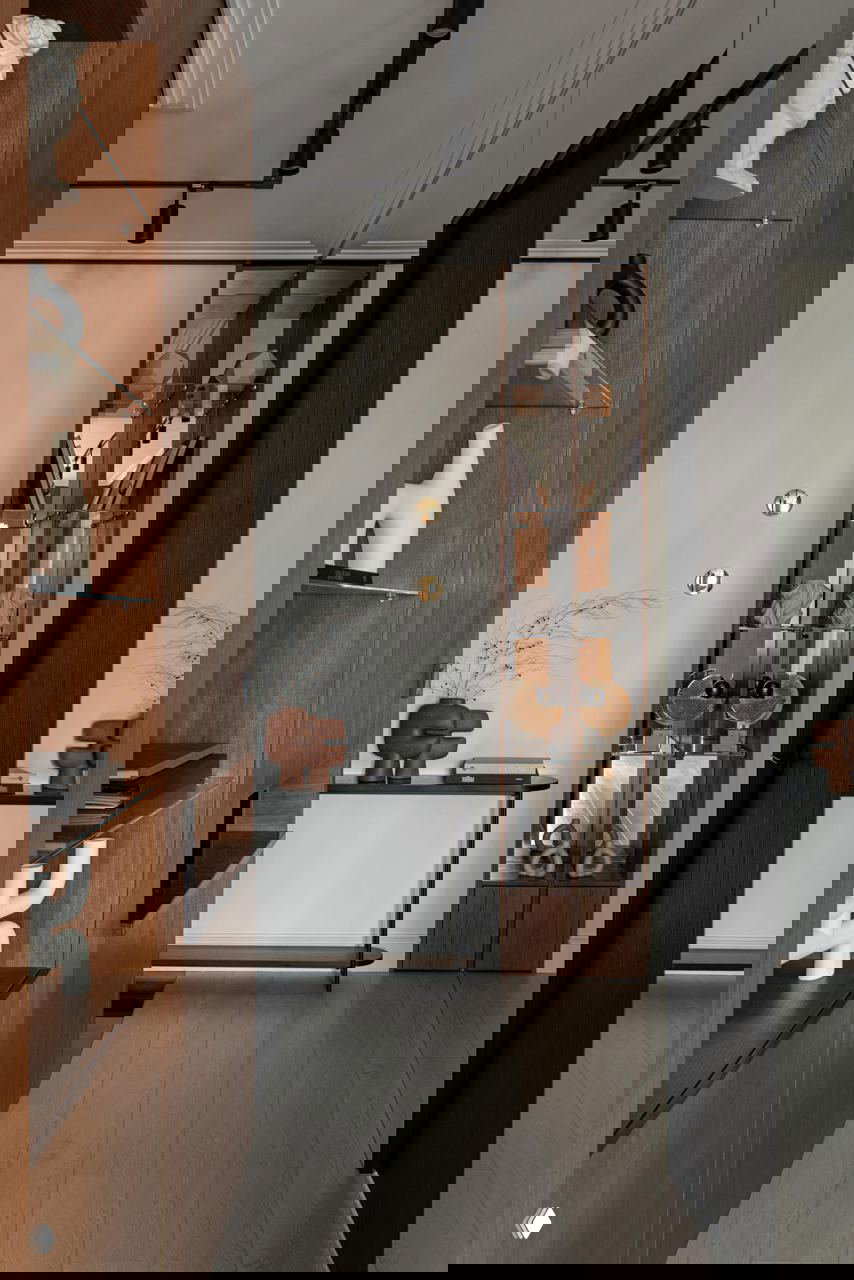 Коридор с деревянными встроенными стеллажами и стеклянной витриной, декоративные скульптуры и зеркальная секция, тёплые древесные оттенки в отделке.