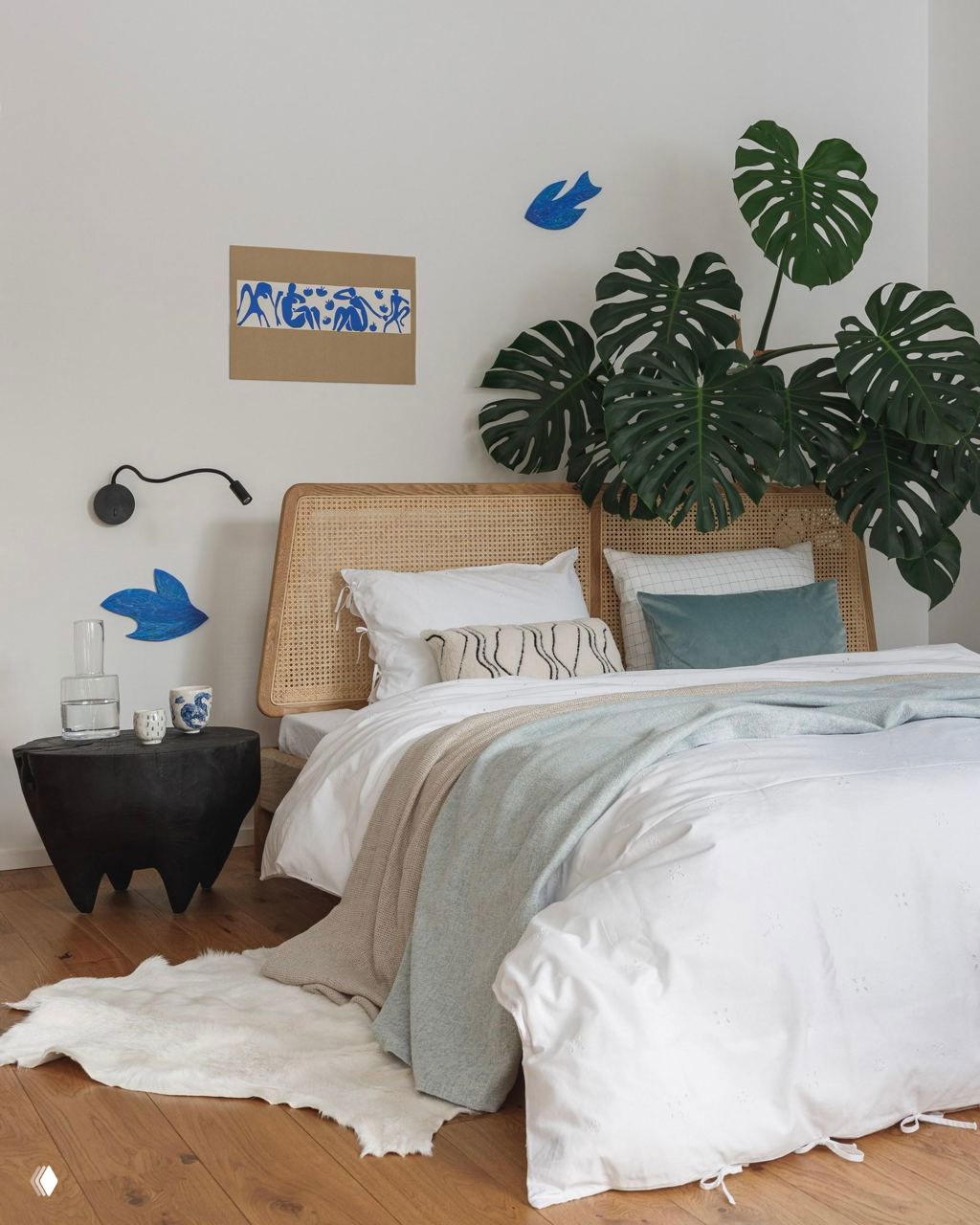 Нежный интерьер спальни с ротанговым изголовьем и большой монстерой рядом с кроватью, светлые текстуры и минимум декора.