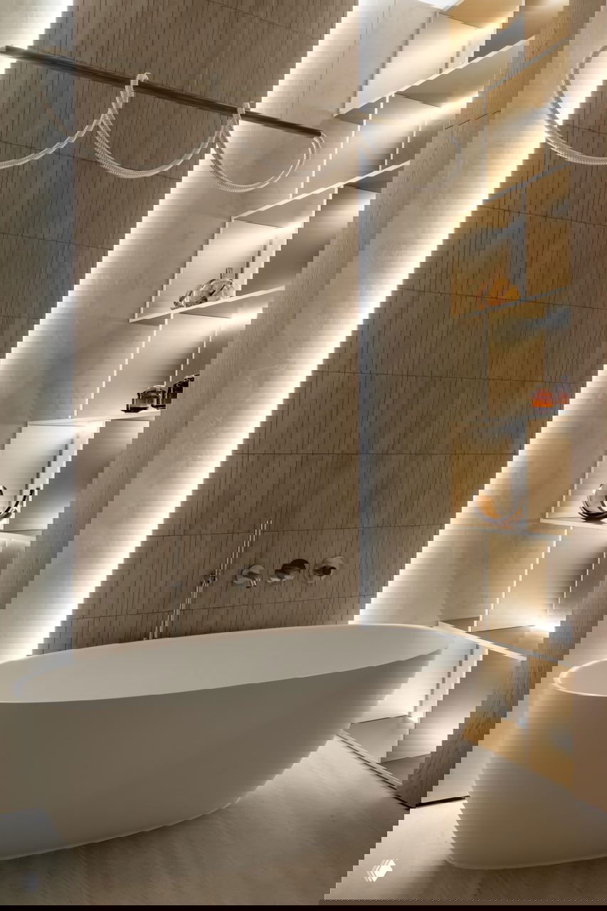 Ванная с отдельно стоящей овальной ванной, подсвеченными нишами для декора и облицовкой натурального оттенка — элегантный и спокойный санузел.