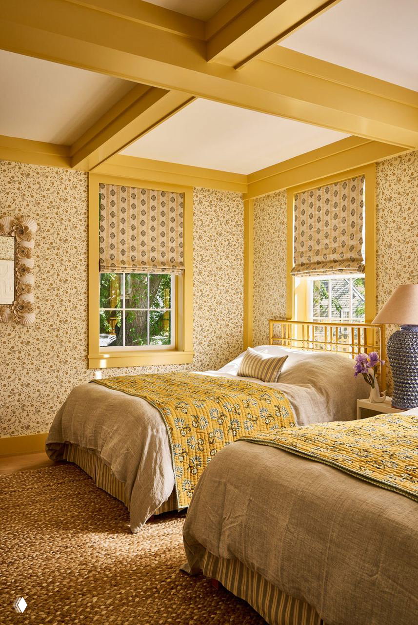Спальня в жёлто‑горчичной гамме: цветочный принт на обоях и текстиле, балочные потолки и натуральные ткани создают тёплую атмосферу.