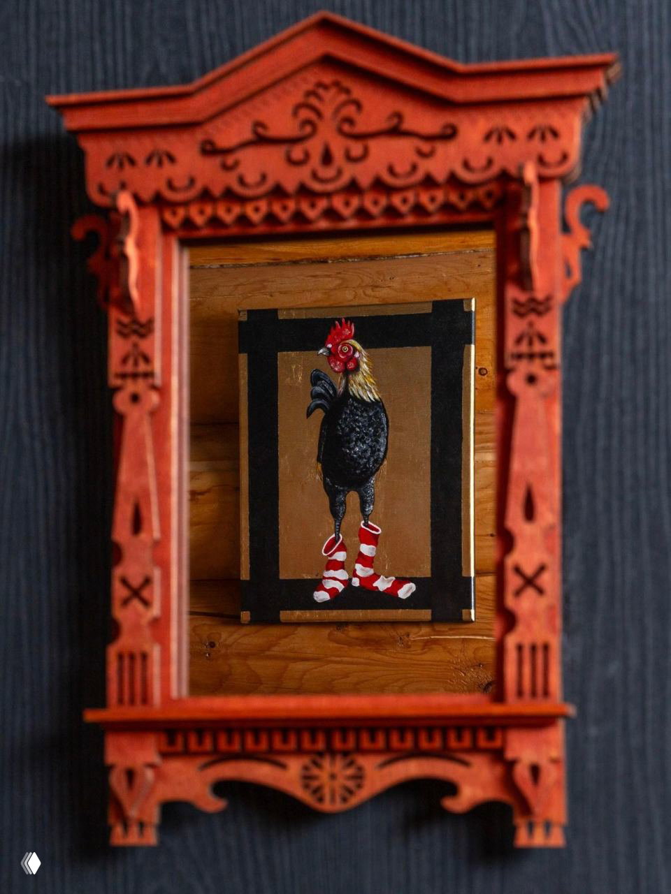 Резное деревянное зеркало в красном цвете на фоне тёмной стены и декоративная картина с изображением петуха в носках — акцентный предмет интерьера в доме