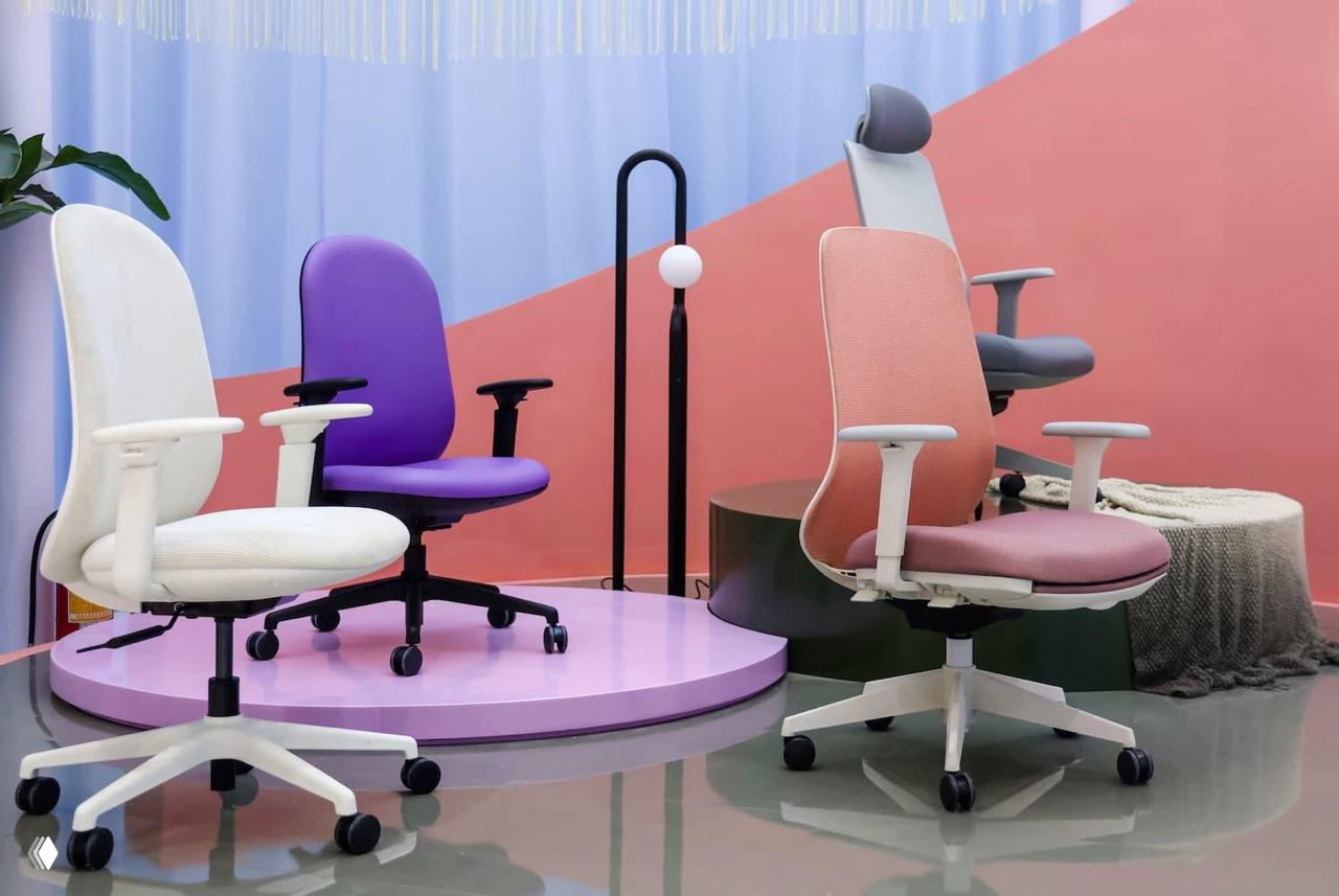 Ряд офисных кресел разных цветов и форм, представленных на выставке как примеры эргономичных решений для офиса.