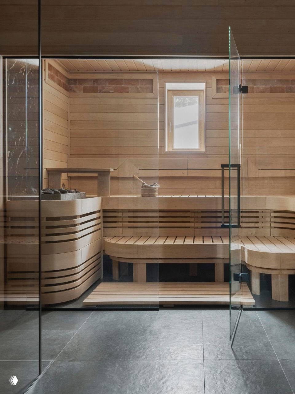 Современная сауна с деревянной отделкой, стеклянной дверью и удобными лавками, выполненная в тёплых натуральных оттенках и строгих линиях.