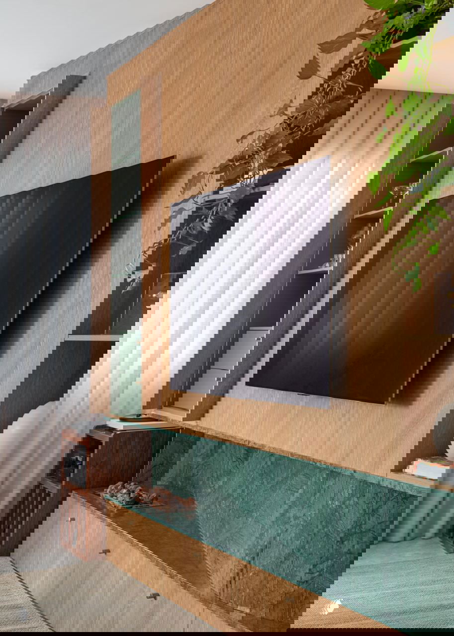 Крупный план телевизора на деревянной стеновой панели, открытая ниша со стеклянной посудой и зелёная мраморная столешница под ним.