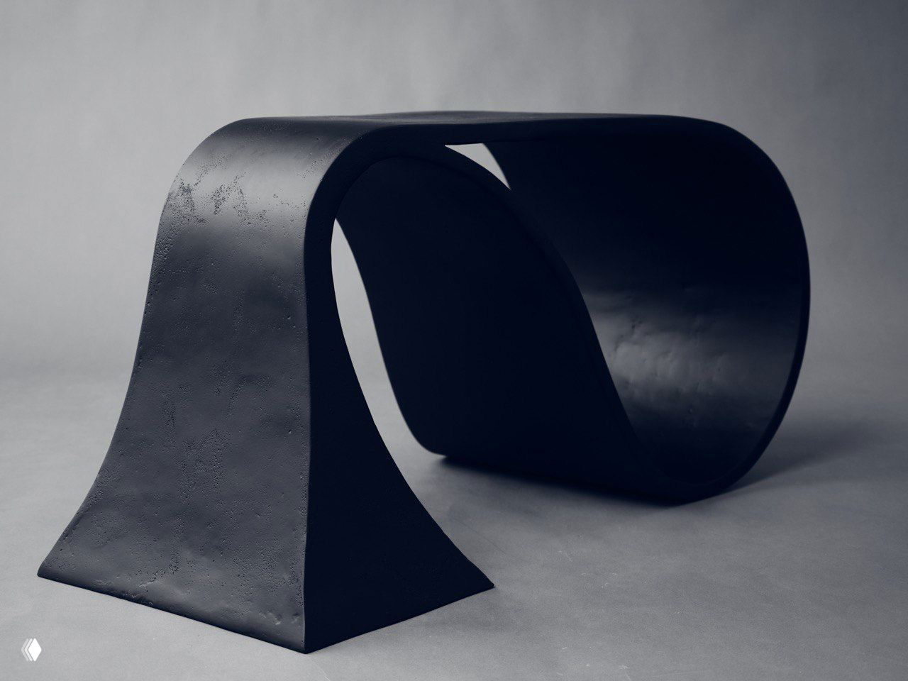 Мини-столик из чёрного окрашенного материала с плавными органическими формами на нейтральном фоне, крупный план поверхности и силуэта предмета.