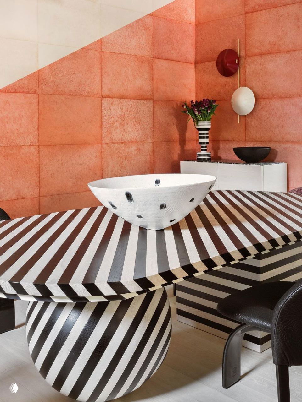 Яркая композиция: стол с чёрно-белыми диагональными полосами, коралловые стеновые панели и декоративная керамическая чаша — смелый графичный акцент в интерьере.