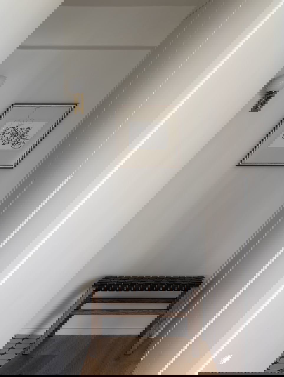 Узкий коридор с простой деревянной скамьёй, рамкой с графическим принтом и настенным светильником — минималистичный вход в квартиру.