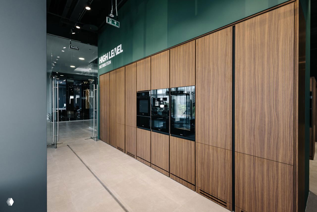 Стена из деревянных панелей со встроенной техникой Asko в шоуруме High Level: модульные шкафы, черные стеклянные дверцы и контраст с тёмным потолком.