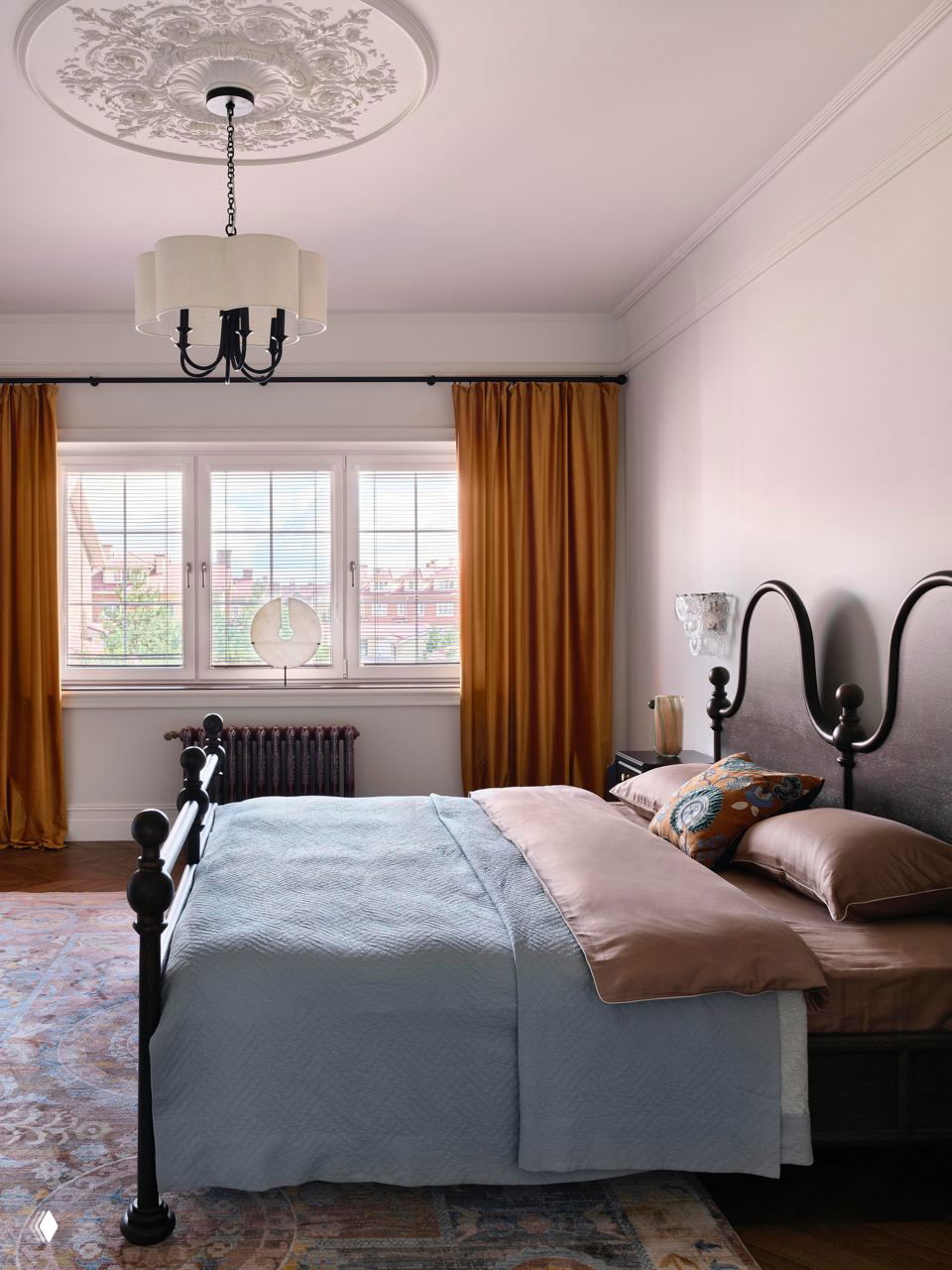 Спальня с чёрной металлической кроватью, голубым покрывалом и горчичными шторами на окне — мягкая классическая палитра и текстуры.