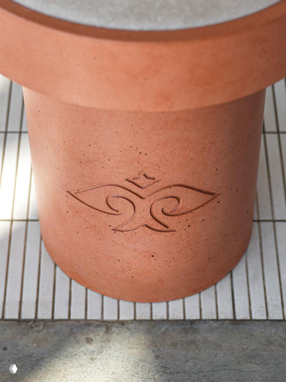 Деталь интерьера: цилиндрическая терракотовая опора со стилизованным орнаментом, демонстрирующая материал и брендинговый знак в оформлении.
