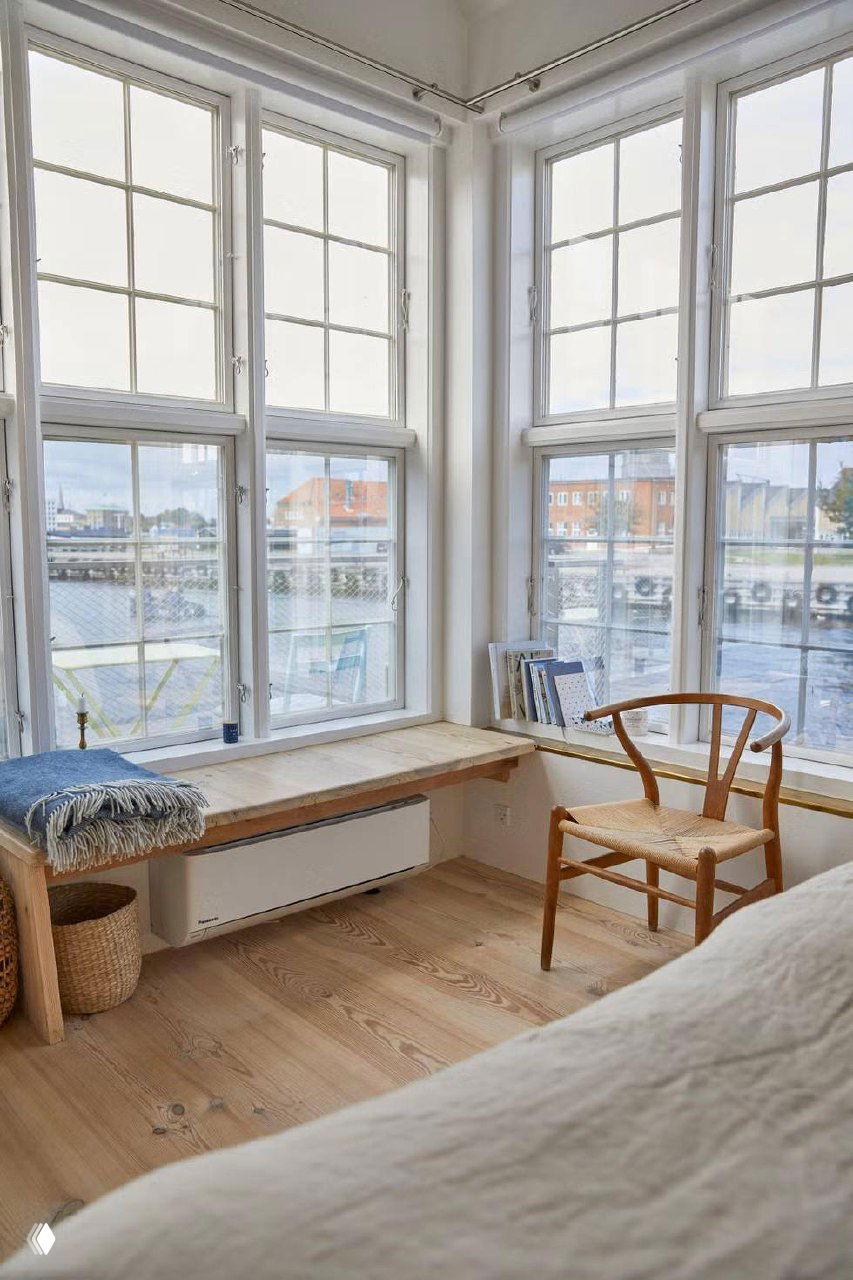 Интерьер номера с большими наклонными окнами, скамьёй у окна и видом на гавань — уютная зона у окна с деревянным полом.