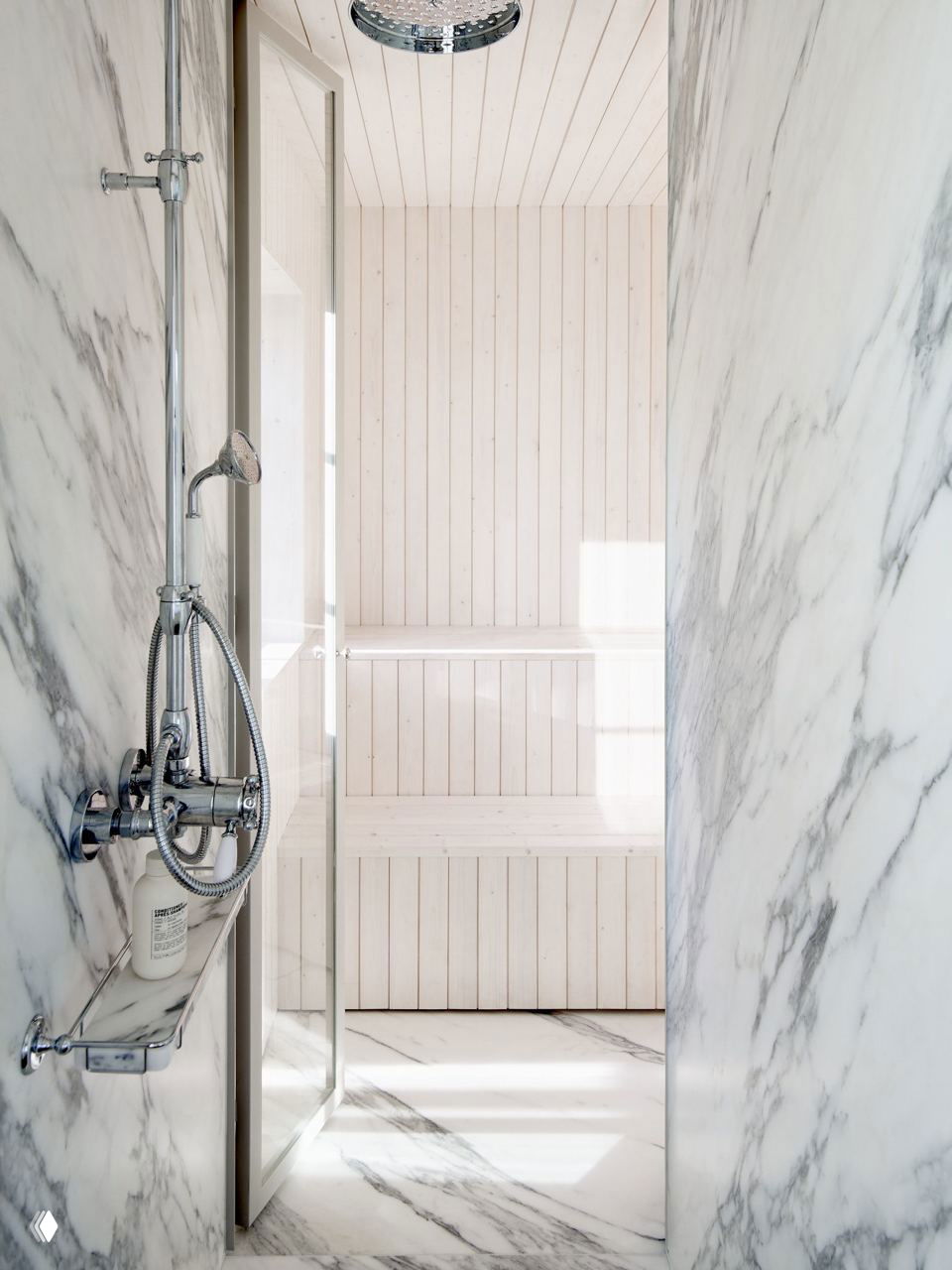 Мраморная душевая и внутренние деревянные панели сауны за стеклянной дверью: сочетание натурального камня и светлого дерева в ванной зоне.