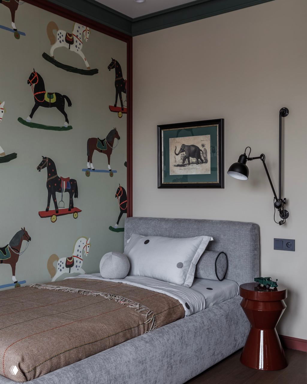 Спокойная спальня мальчика с обоями с лошадками, серой кроватью и настенным светильником — классический детский интерьер с винтажными мотивами.
