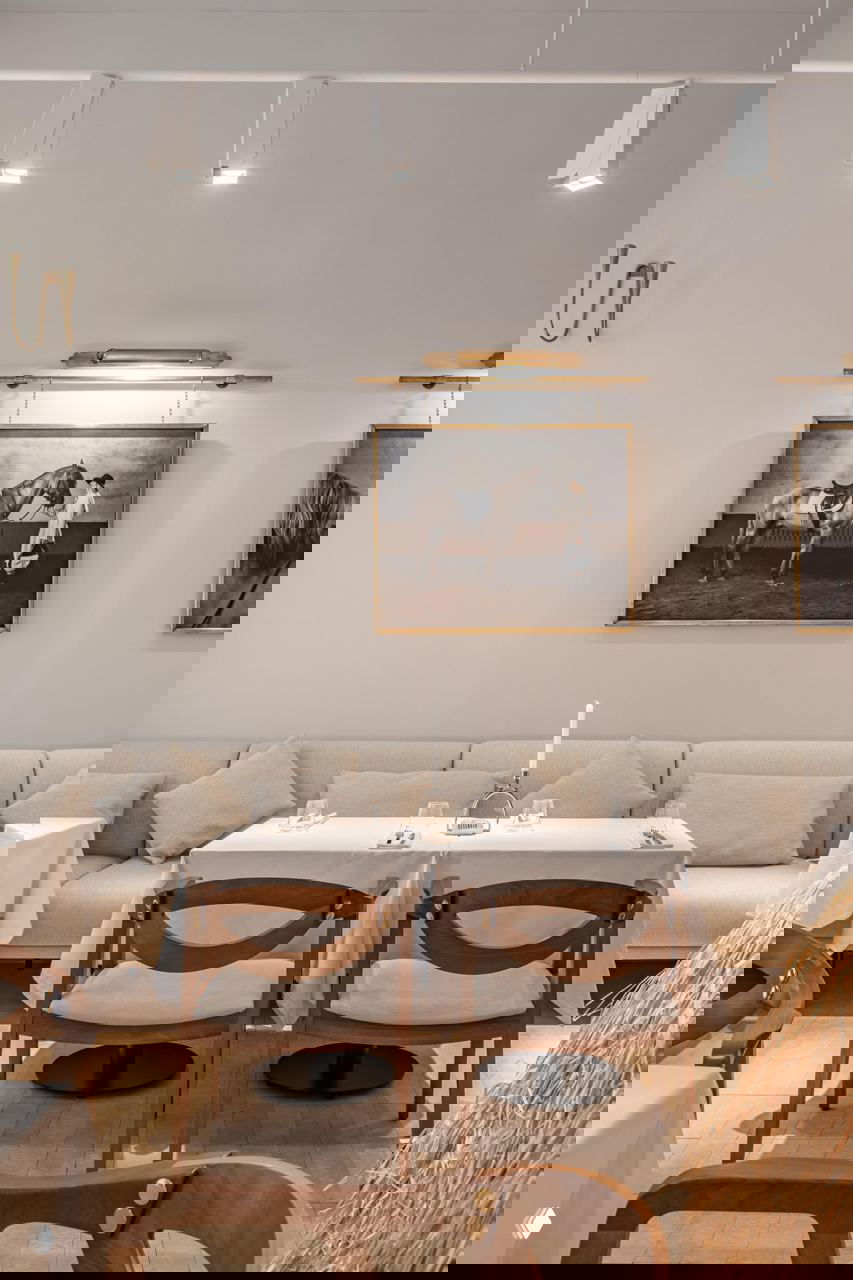 Интерьер брассери Savras с мягкой банкеткой, деревянными стульями и картинами с изображением лошадей над диваном в спокойной цветовой палитре.