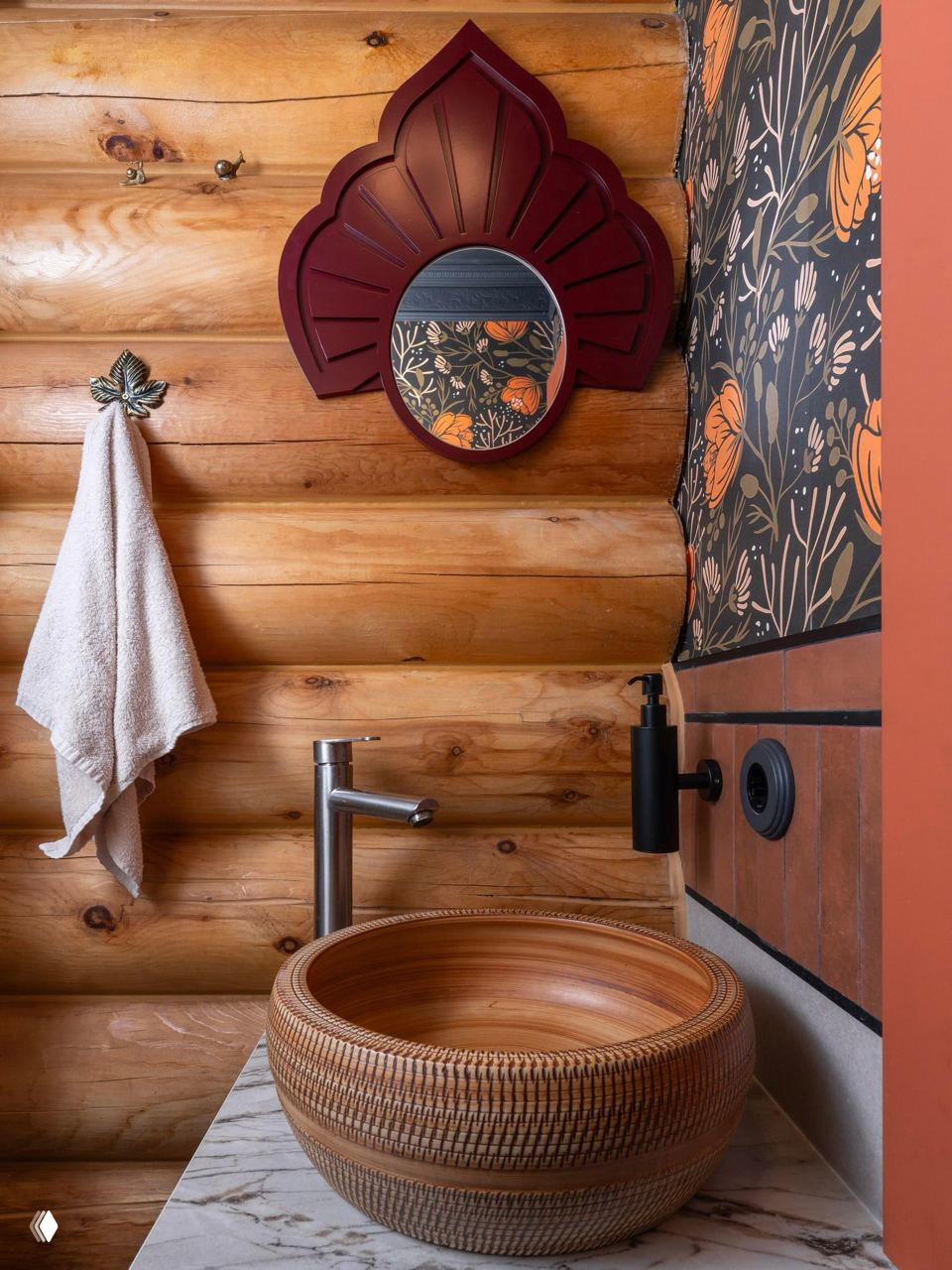 Маленькая ванная комната: деревянные бревна, круговое резное зеркало бордового цвета и плетёная раковина на мраморной столешнице — традиция в современной интерпретации