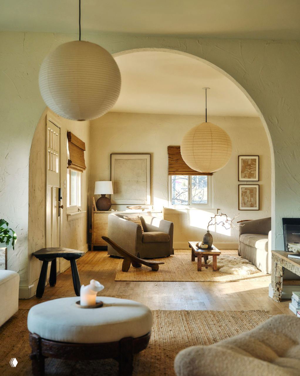 Вид через большую арку на зону отдыха с диванами, подвесными бумажными светильниками и низким столиком в нейтральной палитре.