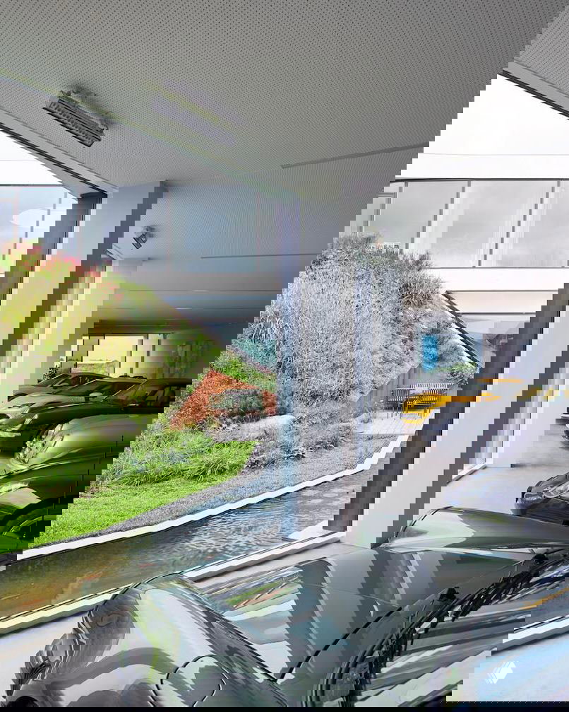 Вид изнутри на часть дома с гаражом: через большие стеклянные окна видна озеленённая терраса и ландшафт, соединённые с внутренним пространством.