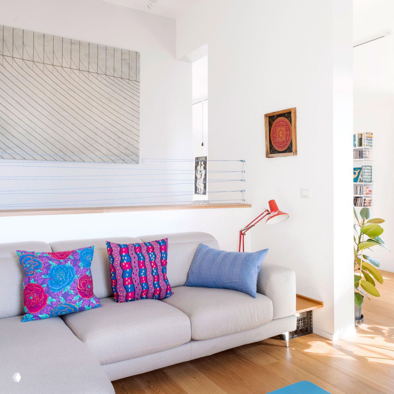 Светлая гостиная с мягким диваном и яркими декоративными подушками, белые стены дополняются акцентами в текстиле и аксессуарах.