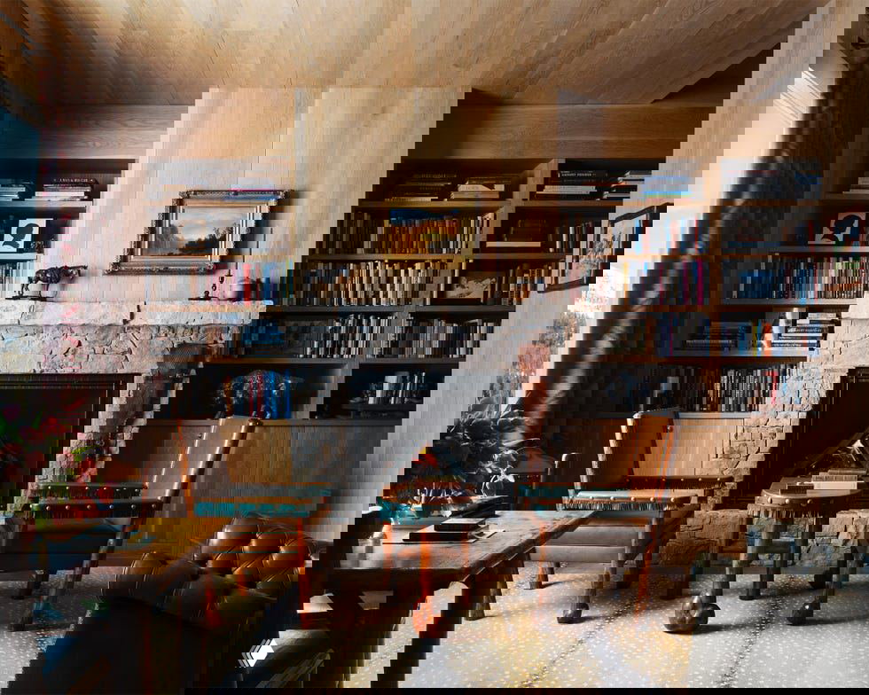 Книжный уголок с камином и встроенными стеллажами, кожаные кресла и журнальный столик на деревянном полу — уютная библиотечная зона в ранчо.