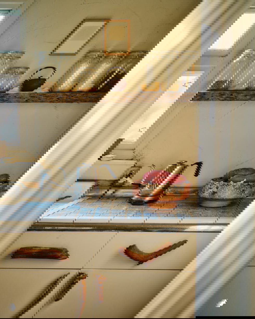 Кухонная рабочая поверхность с синими плитками, деревянными ручками на шкафах, металлическим чайником и миской с продуктами, натуральные фактуры.