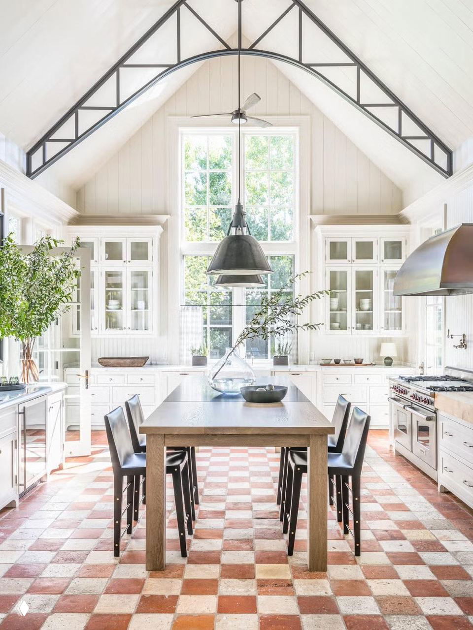 Светлая просторная кухня-столовая с высокими окнами и красно-белой шахматной плиткой на полу, длинный деревянный стол посередине