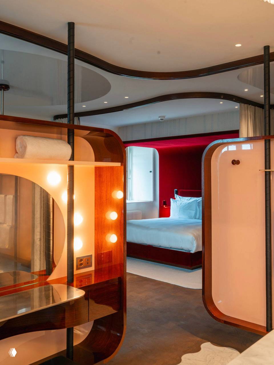 Люксовая спальня нового крыла: изогнутые деревянные перегородки, ретро-зеркало с подсветкой, мягкие текстуры и кровать с насыщенно-красной отделкой в глубине.