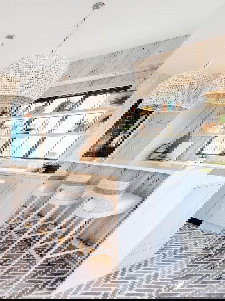 Светлая кухня с барной стойкой и плетёными подвесными светильниками, пол выложен плиткой в узор «ёлочка» из кирпича или камня