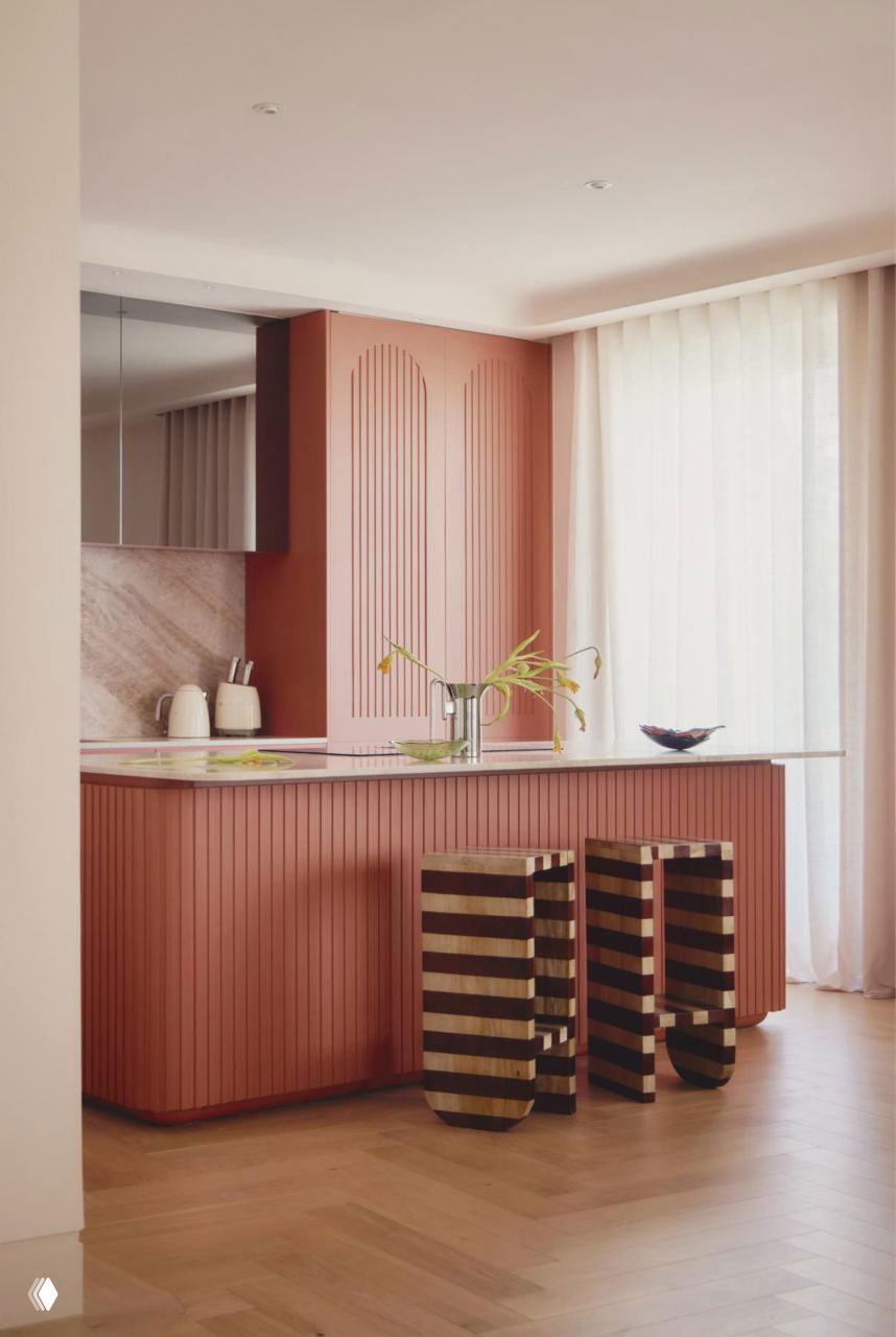 Кухонный остров тёплого терракотового оттенка с декоративными стульями в полоску и мягким дневным светом через полупрозрачные шторы.