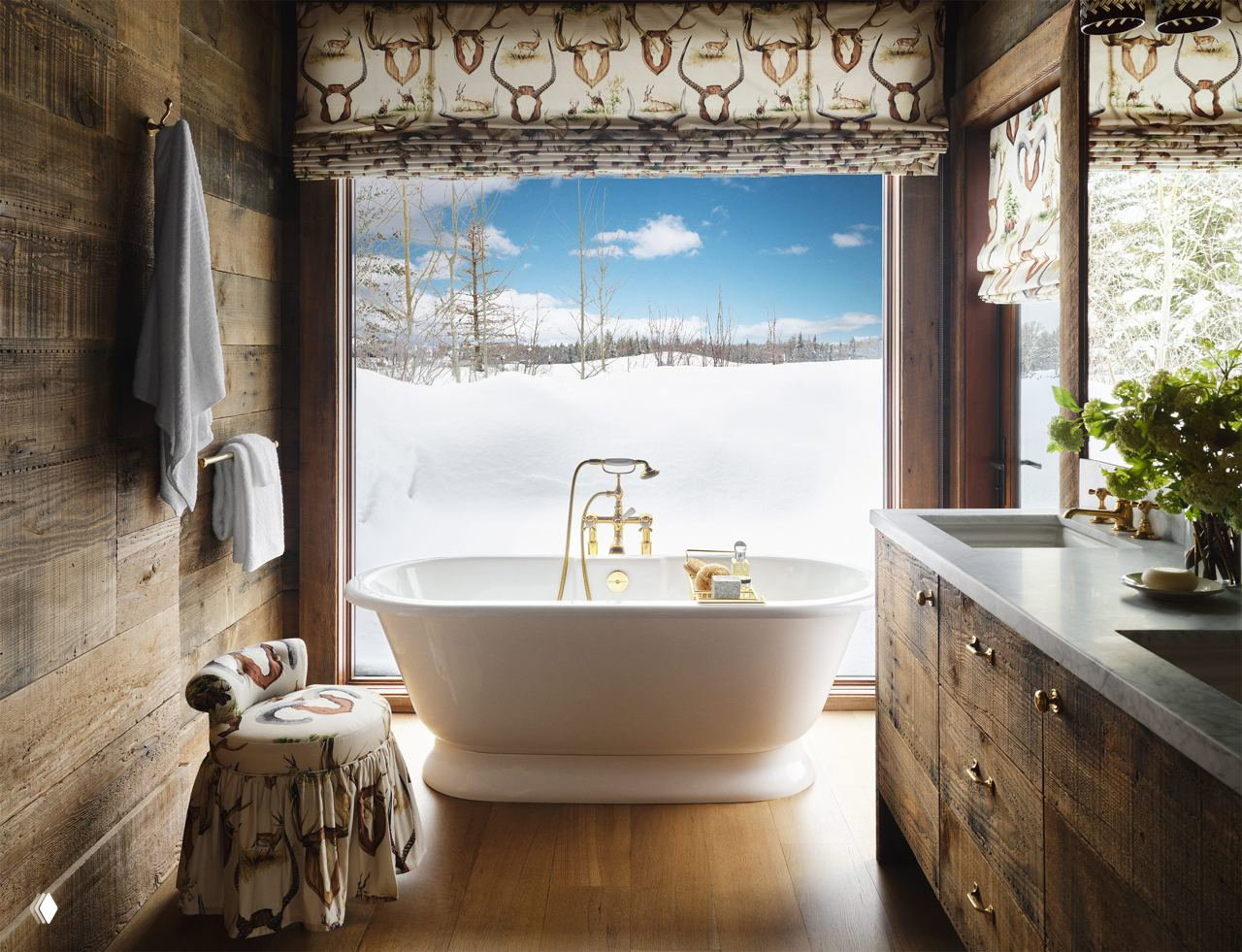 Ванная комната с отдельно стоящей белой ванной у большого окна: вид на заснеженный пейзаж, латунная сантехника и деревянная отделка создают атмосферу ранчо.