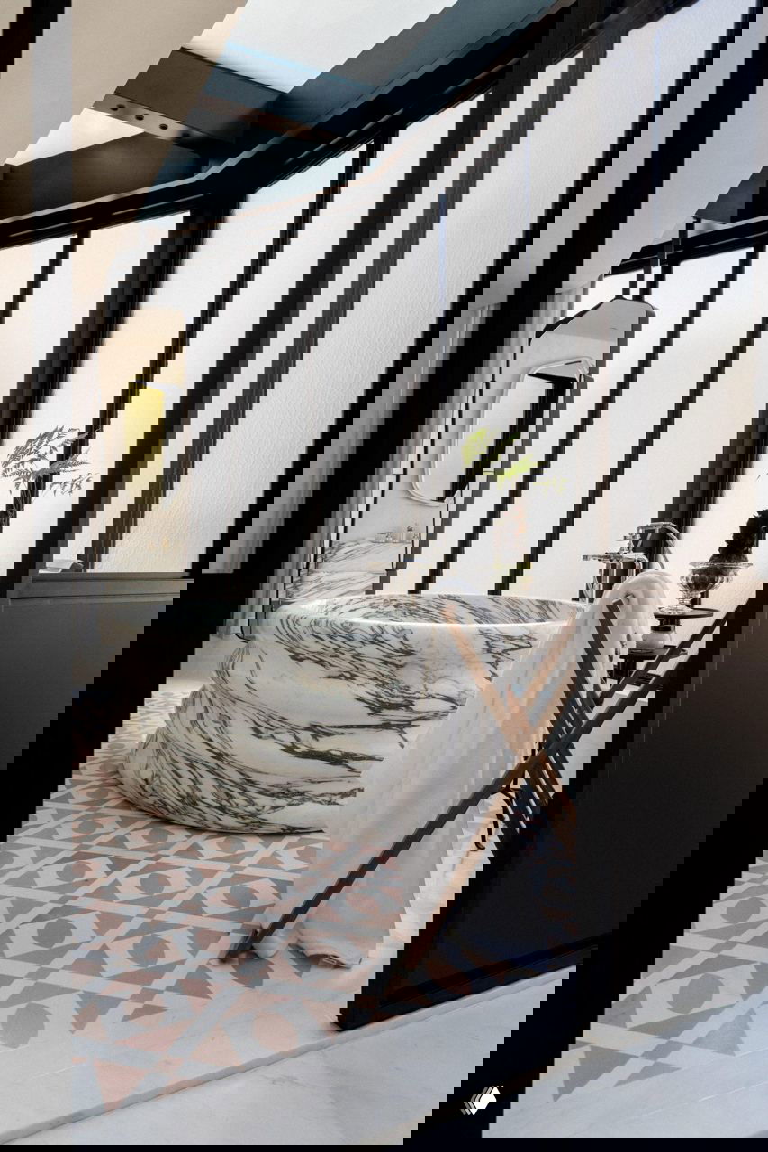 Ванная с округлой мраморной ванной и матовым стеклом, естественный свет фильтруется через высокие окна, подчёркивая рисунок камня.