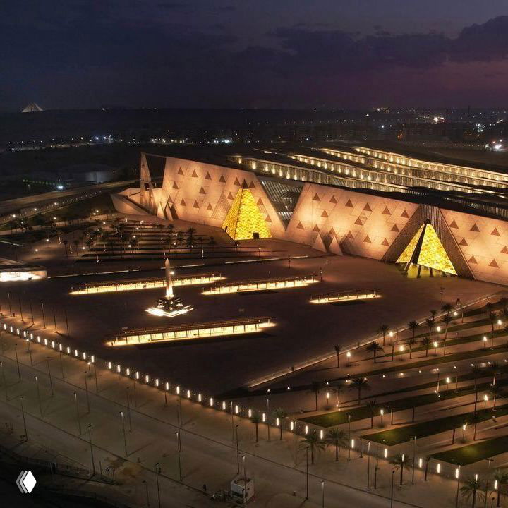 Ночной вид на современный музейный комплекс с треугольными светящимися фасадами и наружной подсветкой, освещённая площадь.