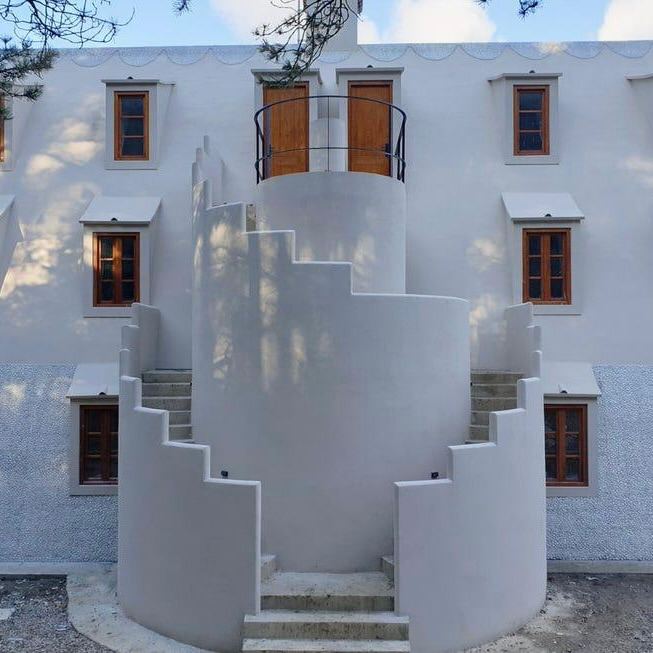 Крупный план криволинейной ступенчатой наружной лестницы у фасада дома, белая штукатурка и тени от сосен.