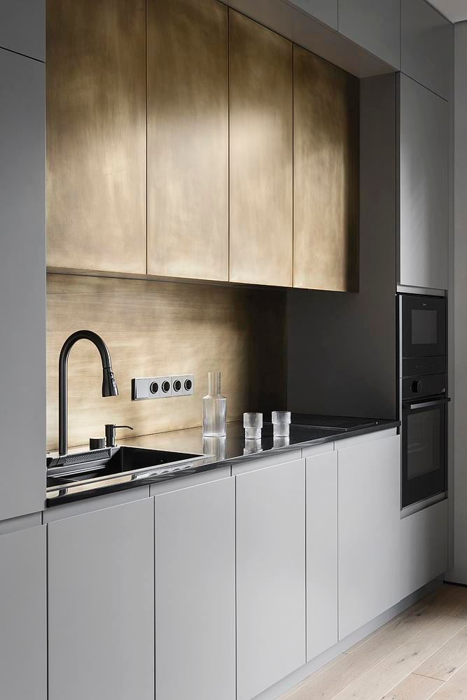 Кухонная рабочая зона с бронзовым фартуком и фасадами, чёрным смесителем и тёмной глянцевой столешницей — акцент на материалах и фактурах.